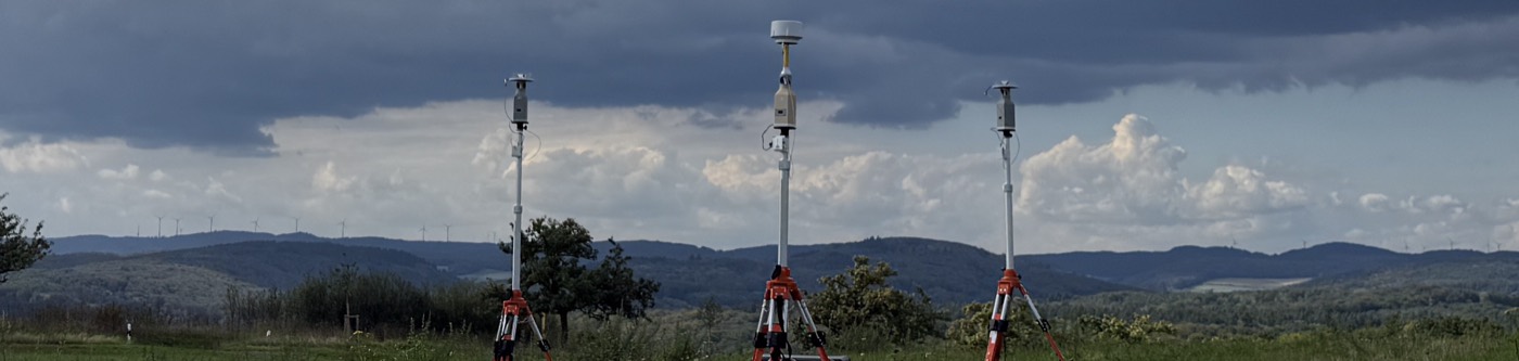 Three antennas on turntables mounted on tripods on an open field